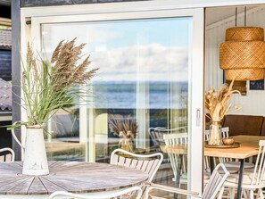 A dining area with a round wooden table and white chairs, a white vase with dried plants, and a wicker lamp. - 6 Person Holiday Home in Faaborg (Faaborg)