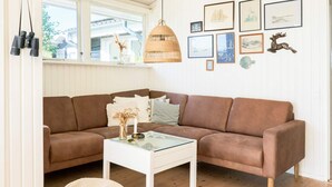 Uma sala de estar com um sofá marrom, uma mesa de centro de vidro e um banquinho de fibra natural.
