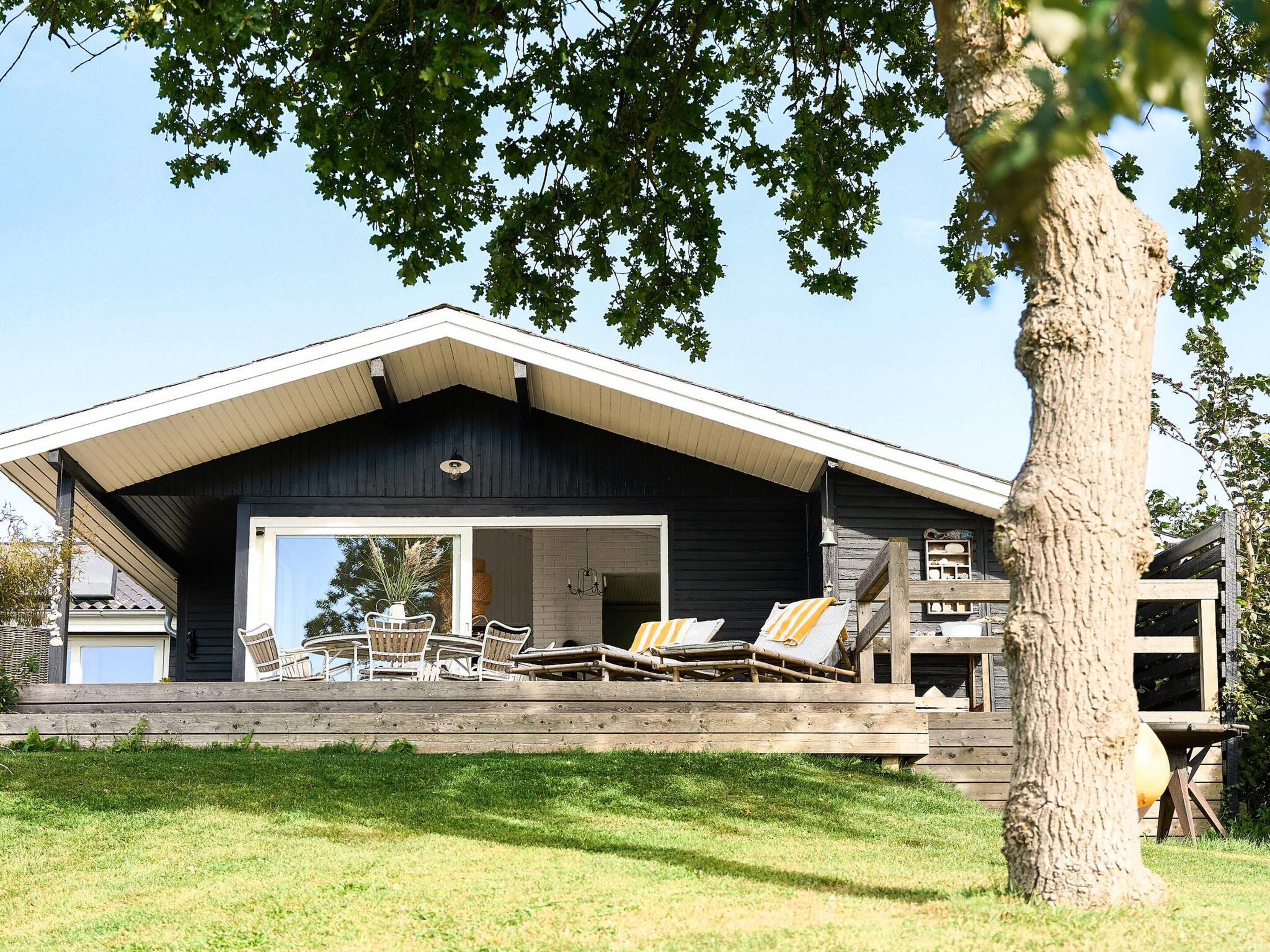 Ein modernes Haus mit einer großen Terrasse, Sitzgelegenheiten im Freien und einem Baum im Vordergrund.