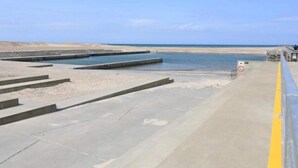 Une zone côtière avec des marches en béton menant à la plage, un ciel dégagé et un panneau indiquant l’interdiction d’accès.