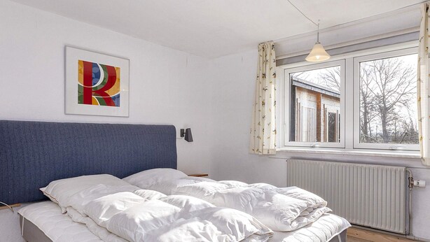 A bedroom with a bed, a window with curtains, a radiator, and a wall-mounted light fixture. - 2 Person Holiday Home in Snedsted (Snedsted)
