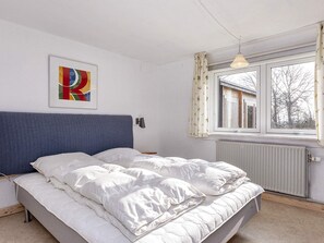 A bedroom with a bed, a window with curtains, a radiator, and a wall-mounted light fixture. - 2 Person Holiday Home in Snedsted (Snedsted)