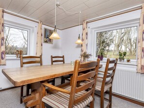 A dining area with a wooden table and chairs, pendant lights, and windows with curtains. - 2 Person Holiday Home in Snedsted (Snedsted)