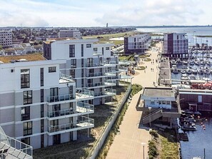 A modern building with multiple balconies, a marina with boats, and a clear view of the water. - Holiday Home in Wendtorf (Wendtorf)