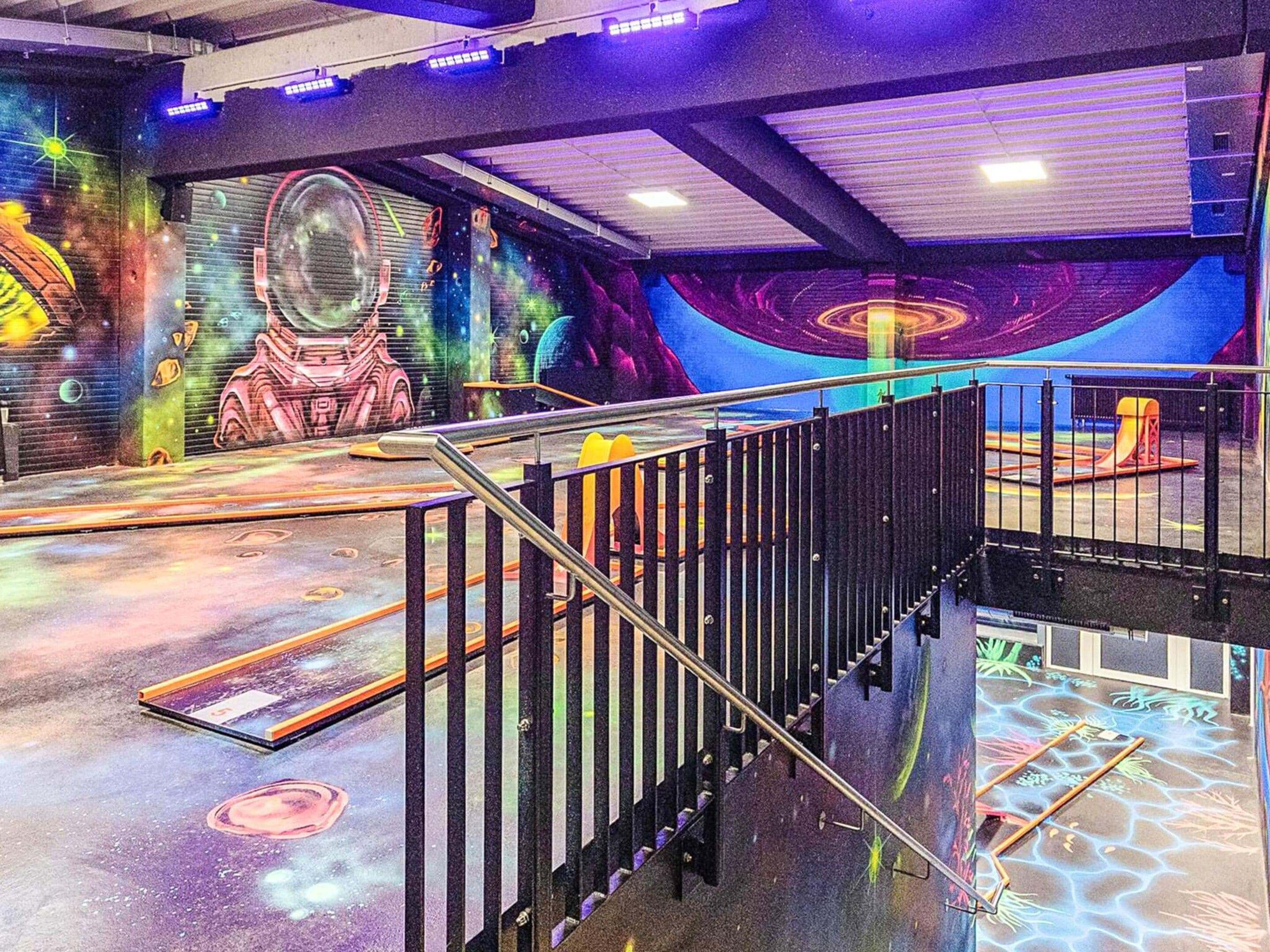 Un espacio interior de varios niveles con escalera, barandas y un mural colorido con temática espacial.