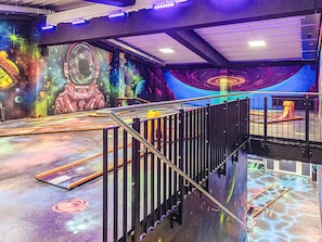 Um espaço amplo e interno com vários níveis, escada, guarda-corpos e um mural colorido com arte temática do espaço.