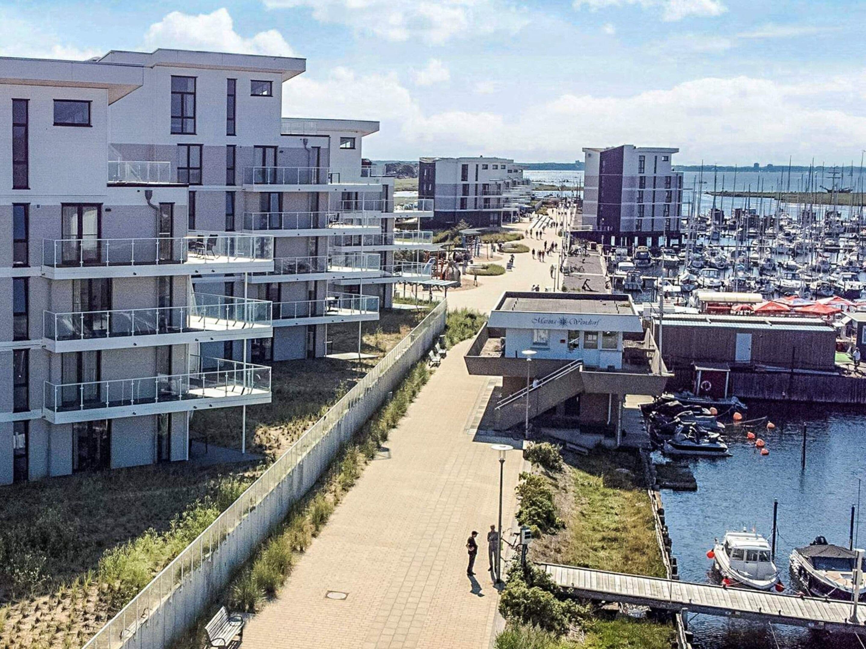Una zona residencial costera con edificios de apartamentos modernos, un puerto deportivo con barcos y un paseo peatonal.