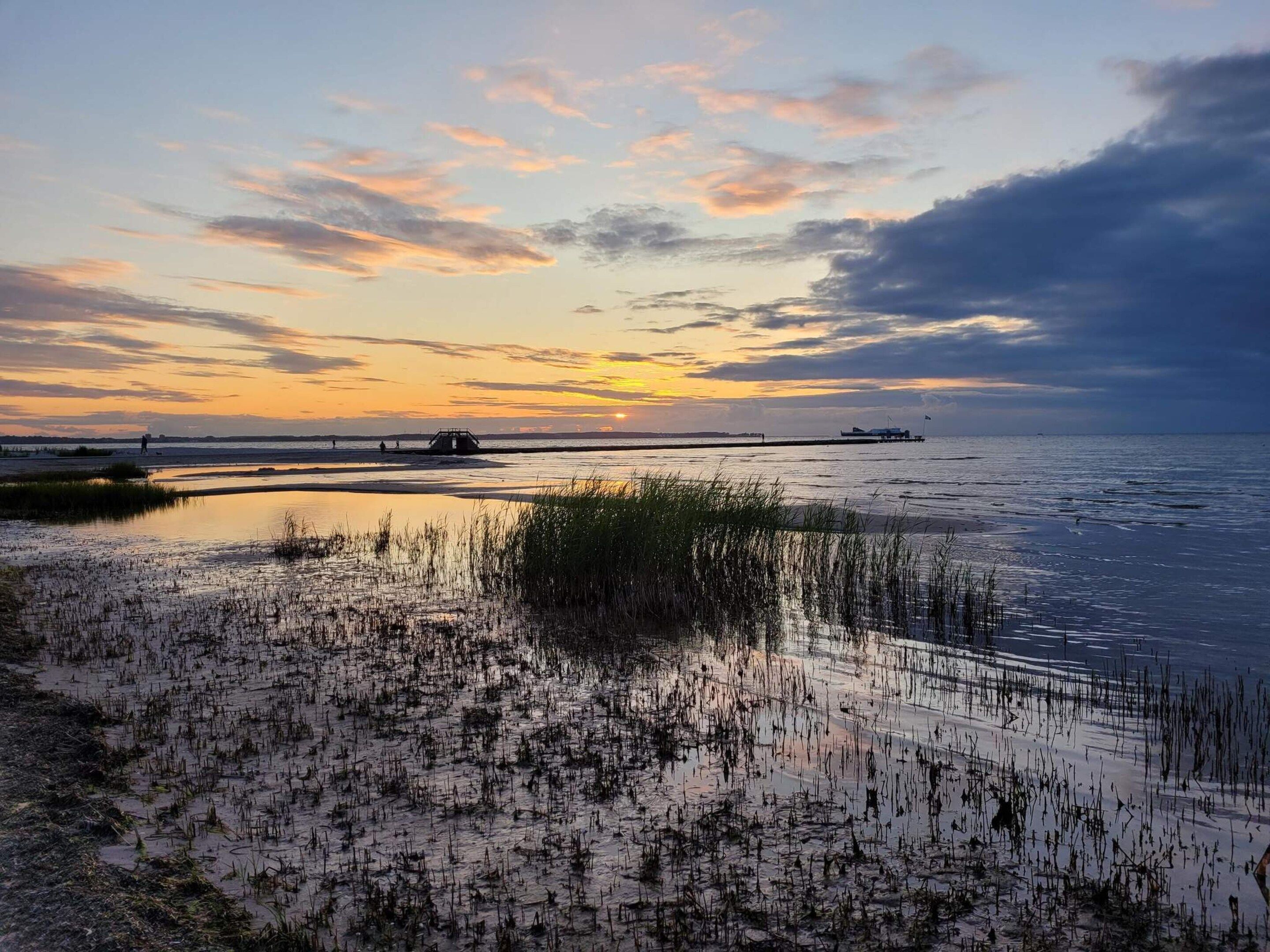 A coastal landscape with a sunset, calm waters, and a pier extending into the sea.