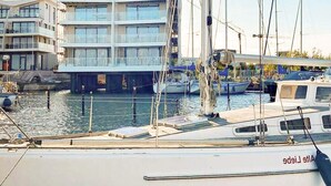 Un port de plaisance avec des bateaux amarrés, un immeuble à plusieurs étages en arrière-plan et un ciel dégagé.