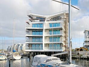 A multi-story building with balconies, a marina with boats, and construction equipment in the background. - Holiday Home in Wendtorf (Wendtorf)