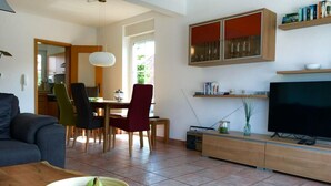 A modern living room with a dining area, a TV, and a kitchen in the background. - Holiday Home Family and dog (Wittmund)