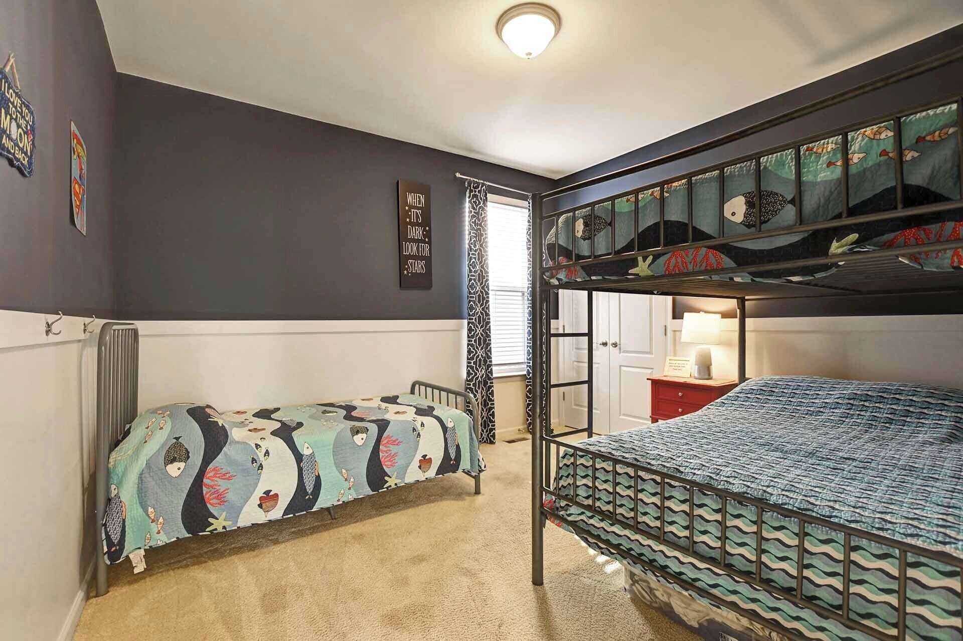 Habitación con literas, una colcha estampada, un radiador, una pared con un cartel y una puerta con cortina decorada.