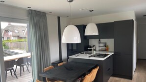A modern kitchen with a central island, pendant lighting, and a dining area with chairs. - Chalet by Water in Idskenhuizen Recreation Park (Idskenhuizen)
