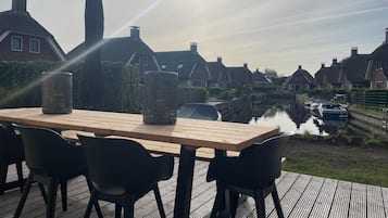 Enjoy a meal in a tranquil outdoor setting with a table and chairs overlooking traditional houses and a serene canal.
