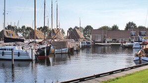 A marina with several boats docked, a grassy area in the foreground, and buildings in the background. - Chalet by Water in Idskenhuizen Recreation Park (Idskenhuizen)
