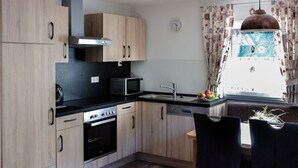 A modern kitchen with wooden cabinets, a stove, microwave, and a dishwasher. There is a dining area with a table and chairs, and a window with curtains. - Nice Apartment in Oberkirch (Oberkirch)
