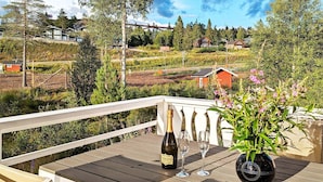 A wooden deck with a bottle of wine and glasses, surrounded by greenery and houses in the background. - 10 Person Holiday Home in Syssleback-by Traum (Sysslebäck)