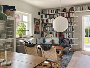 Un salon chaleureux avec une bibliothèque, un canapé, une table à manger et un luminaire suspendu.