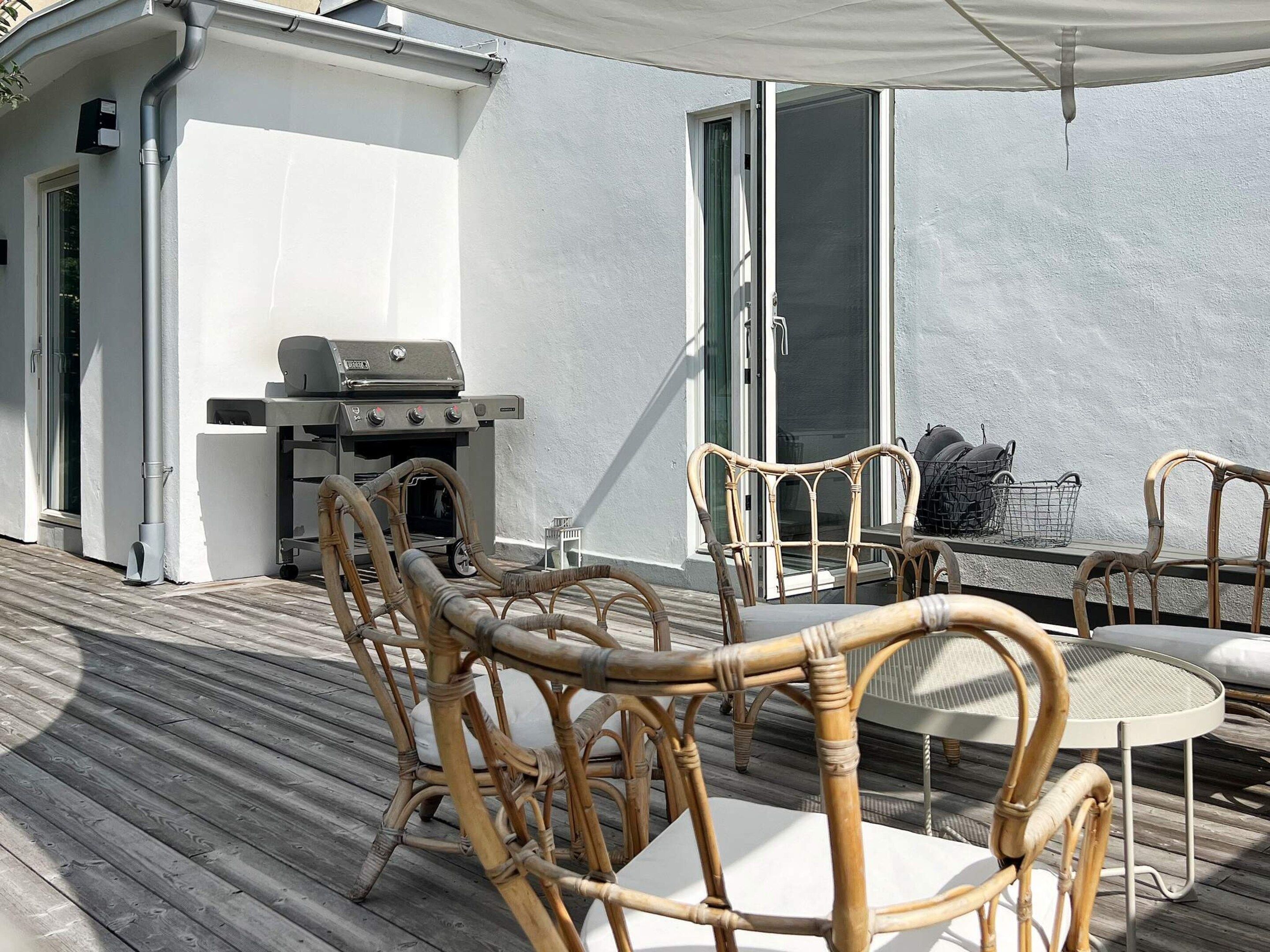An outdoor deck with a grill, wicker chairs, and a table.
