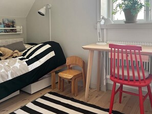 Une chambre à coucher comprenant un lit, un bureau, une chaise, une lampe, un radiateur et une fenêtre avec une plante.