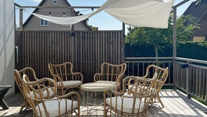 Um deck de madeira com móveis de vime e um toldo branco.