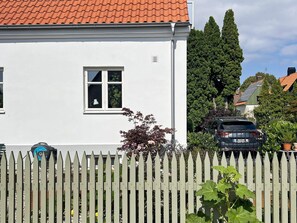 A white house with a red-tiled roof, a white picket fence, and a parked car in front.