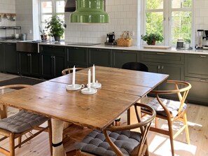 Une cuisine moderne avec des meubles de couleur sombre, une table à manger en bois avec des chaises rembourrées et un luminaire suspendu vert.