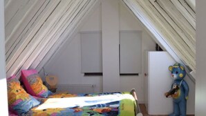 Een slaapkamer met een schuine balkenlaag, een bed met kleurrijk beddengoed, een klein tapijt en een teddybeerbeeldje.