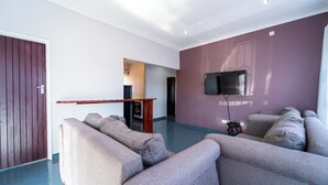 Una sala de estar moderna con un amplio sofá gris, un televisor de pantalla plana montado en la pared y una mesa de centro de madera.