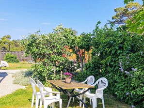 En udendørs terrasse med et bord og stole, omgivet af grøn vegetation og et træhegn.