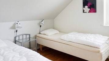 A single bed with a white mattress and pillow, a bedside table with a lamp, and a small metal rack.