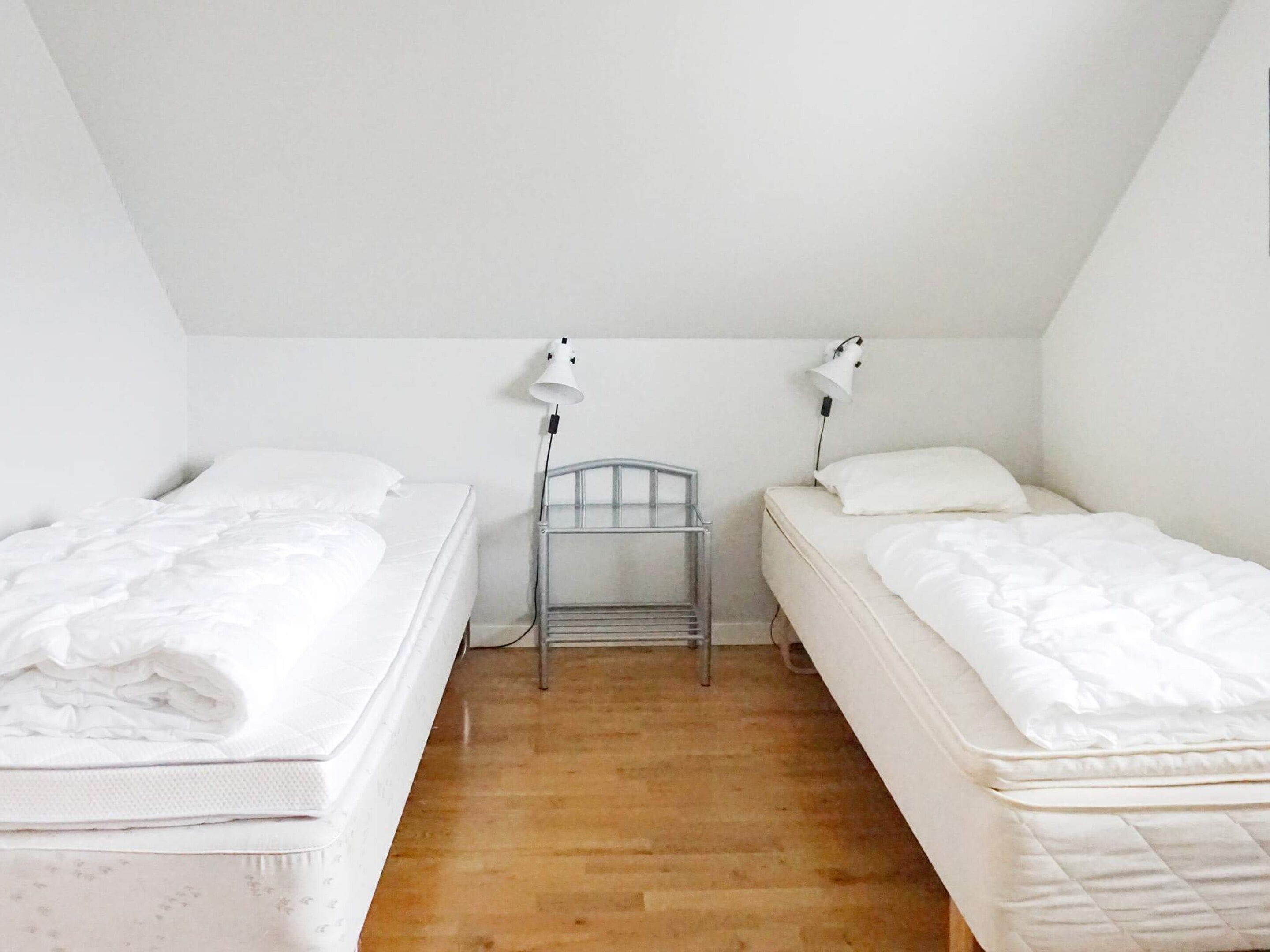 A small, clean room with two single beds, a metal nightstand, and two wall-mounted lamps.