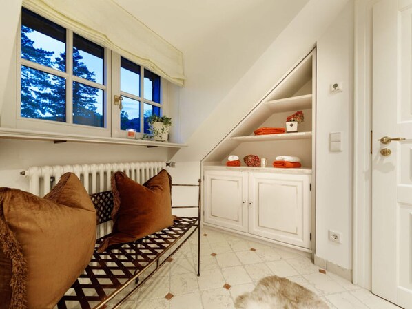 A cozy room with a bench, white cabinets, a radiator, and a window with a view of trees.