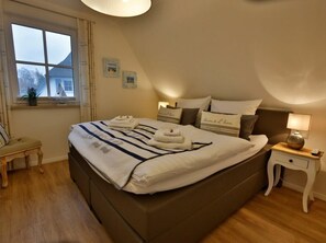 A neatly arranged bedroom with a large bed, bedside tables, a window with curtains, and a view of a house outside. - Seeschwalbe Modern Retreat (Fuhlendorf)
