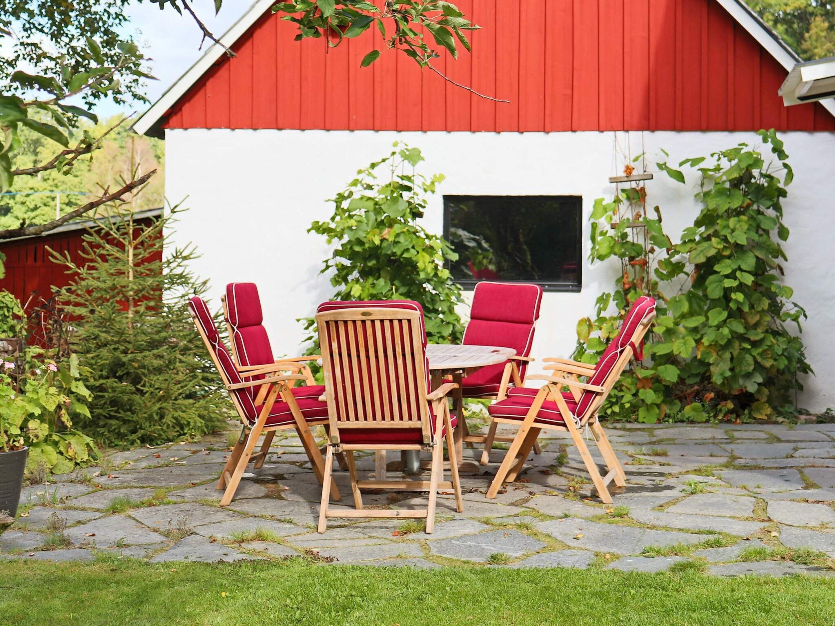 A red barn with a white exterior, a stone patio, and a table with four red chairs.