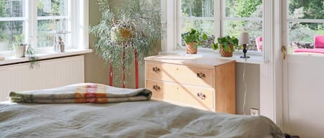 Une chambre à coucher avec un lit, une commode et des fenêtres ornées de plantes.