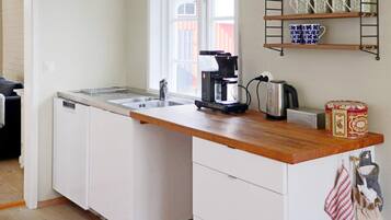 A compact kitchen with a built-in dishwasher, a coffee maker, and a kettle on the countertop.