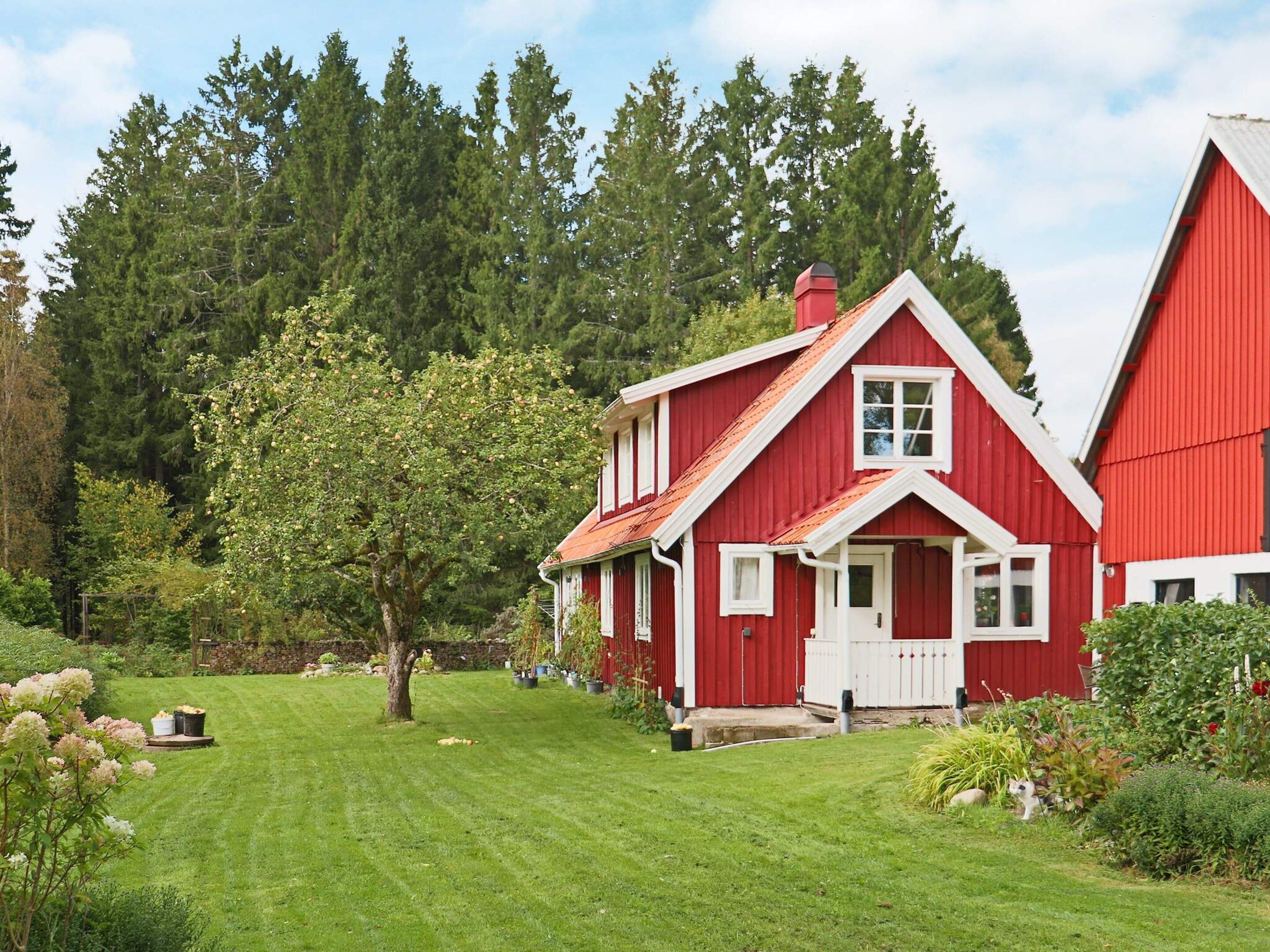 A red two-story house with a white door and windows, surrounded by a well-maintained lawn and trees.