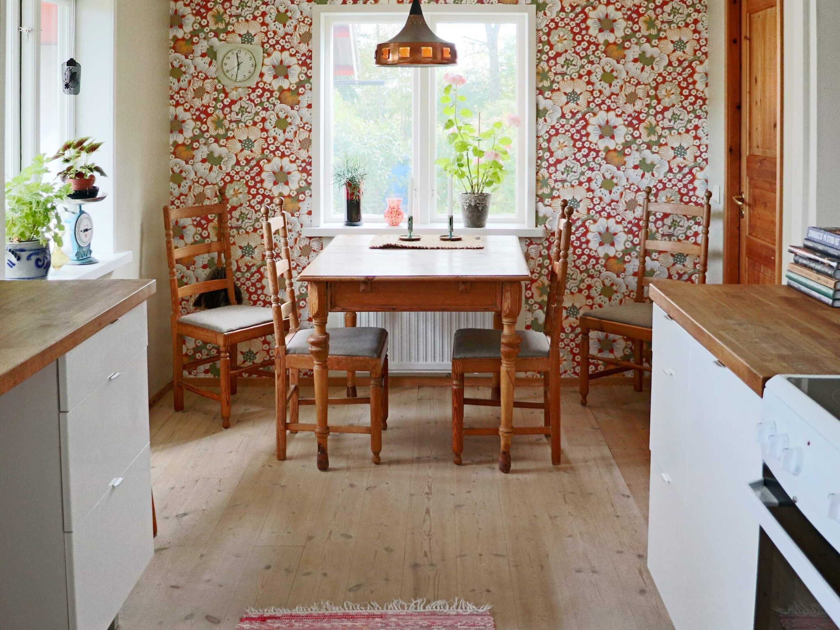 Ein Essbereich mit Holztisch und -stühlen, einem Fenster mit Blick und floraler Tapete.