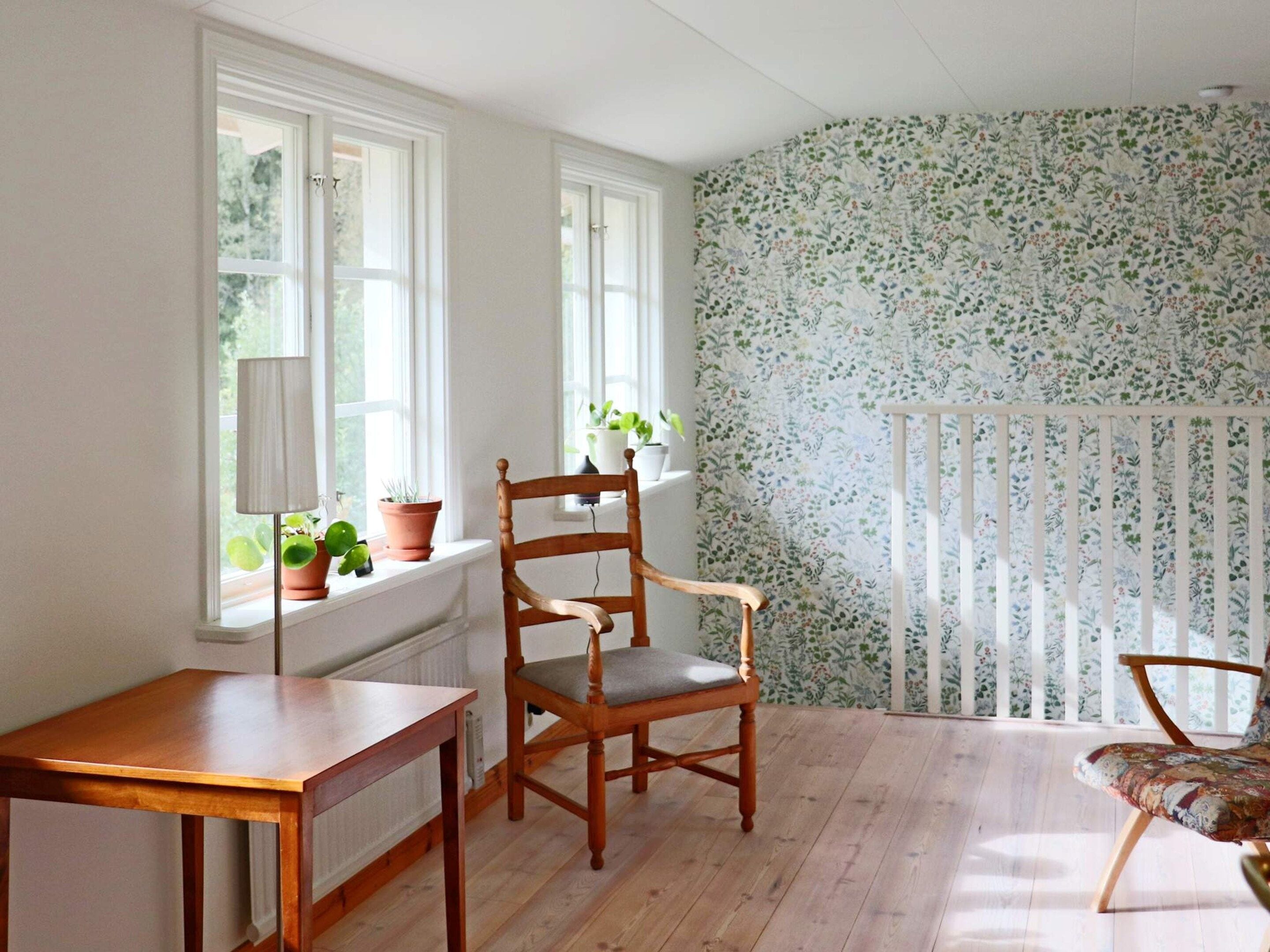 A room with a wooden chair, a small table, and a window with potted plants.
