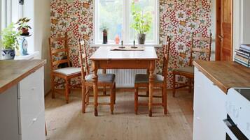 A dining area with a wooden table and chairs, surrounded by floral wallpaper, and a window with plants.