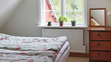 Un dormitorio con una cama, un aparador, un espejo y una ventana con plantas.
