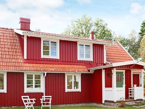 A red two-story house with a red roof, white trim, and a small porch with a green door. - 8 Person Holiday Home in Hishult (Hishult)