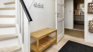 Una escalera con un banco de madera, un perchero y una puerta que da a una zona de cocina.
