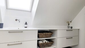Un baño moderno con tragaluz, muebles blancos, un lavabo y una ventana pequeña.