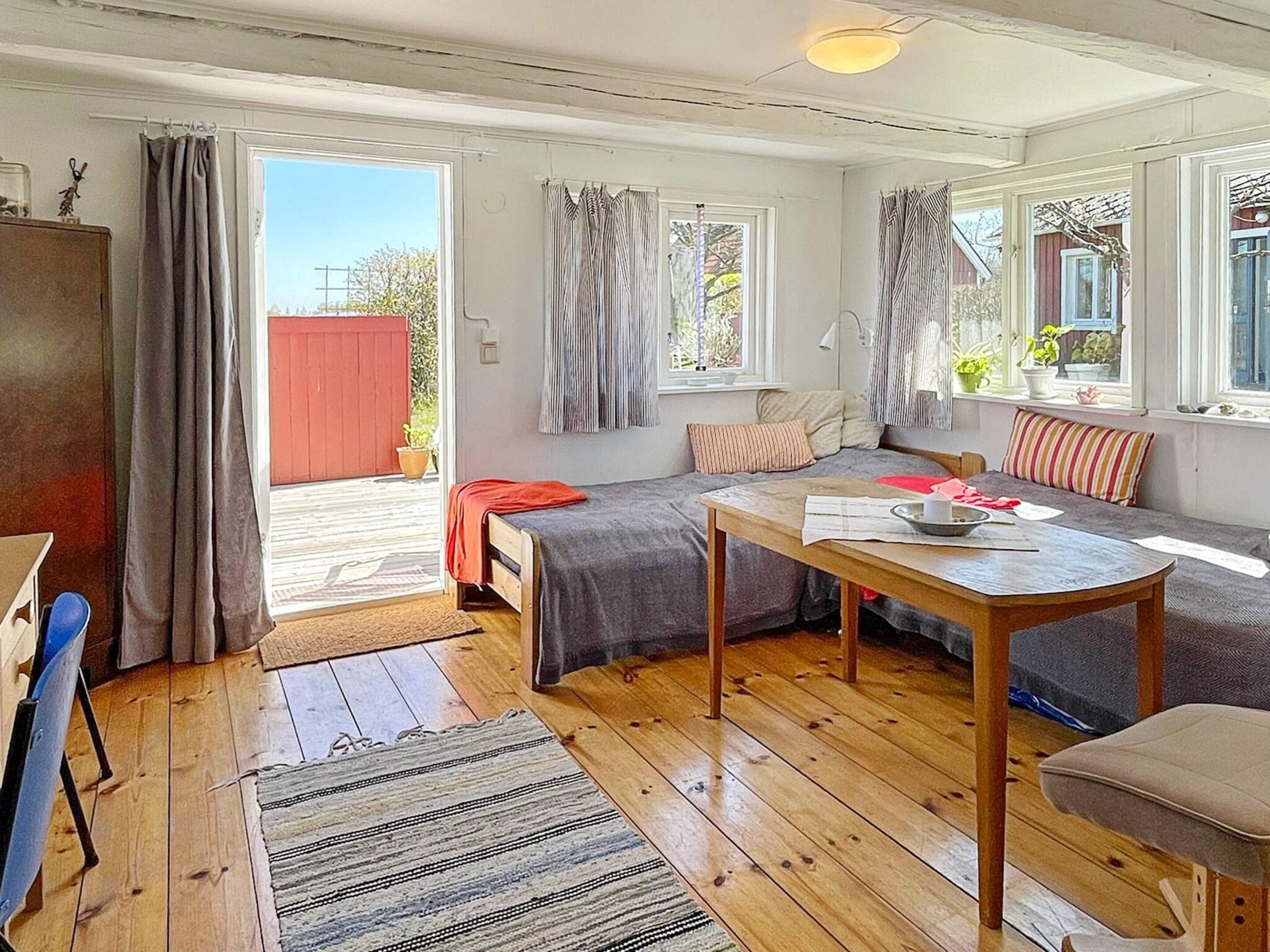 Una habitación acogedora con una cama, una mesa y un sofá. Hay una ventana con cortinas, una puerta que da al exterior y una pequeña mesa con objetos encima.