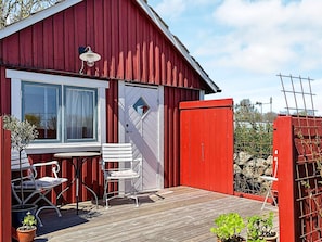 Un bâtiment en bois rouge avec une porte blanche, une fenêtre avec des rideaux et une petite table avec deux chaises à l’extérieur.