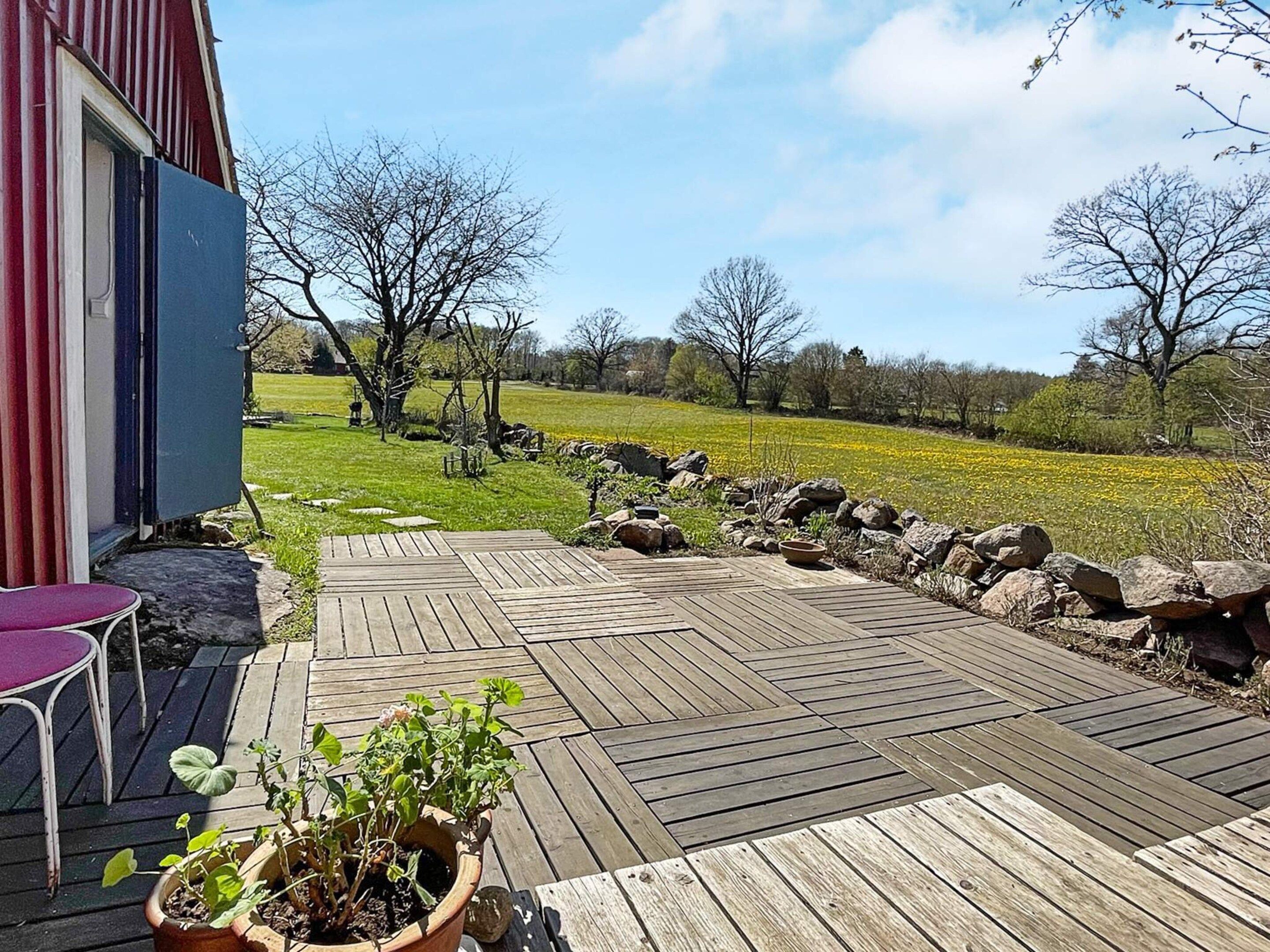 A wooden deck with a potted plant, a red chair, and a stone wall.