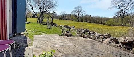 Une terrasse en bois avec un pot de fleurs, une chaise rouge et un mur en pierre.