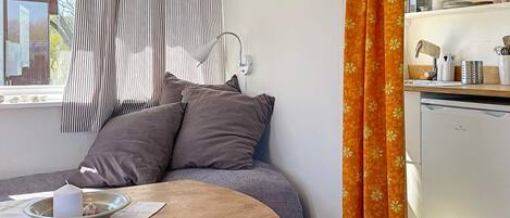Um quarto acolhedor com uma cama, uma mesa pequena com uma vela e uma cozinha equipada com lava-louças.